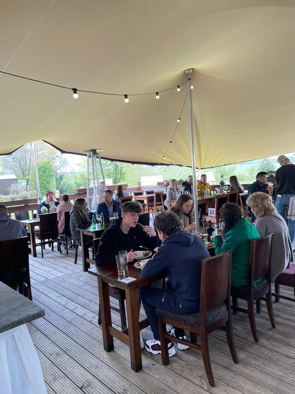Guests dining beneath a cream stretch tent on a covered restaurant terrace with festoon lighting