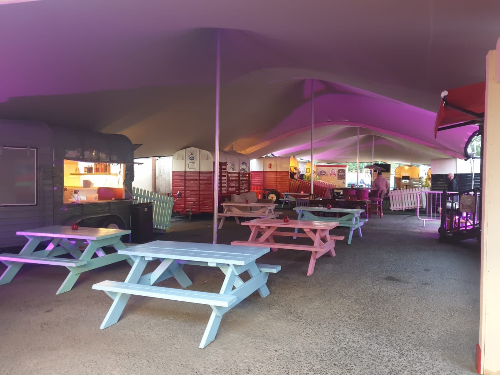 Interior view of a stretch tent covering pastel picnic benches and food vendors with purple ambient lighting
